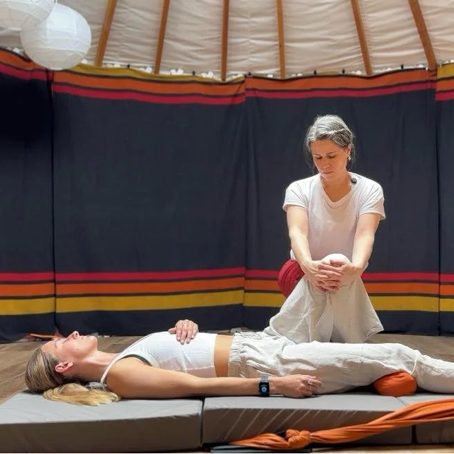 Person receiving a massage in a yurt-like setting with a person standing above them.