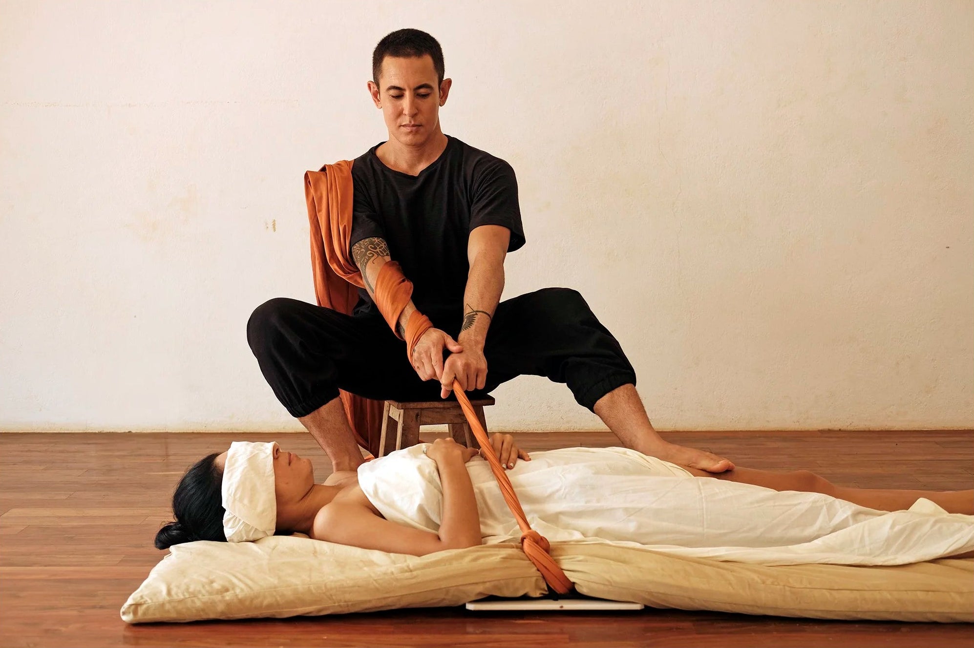 Man giving a massage to a woman on a wooden floor with a plain wall background